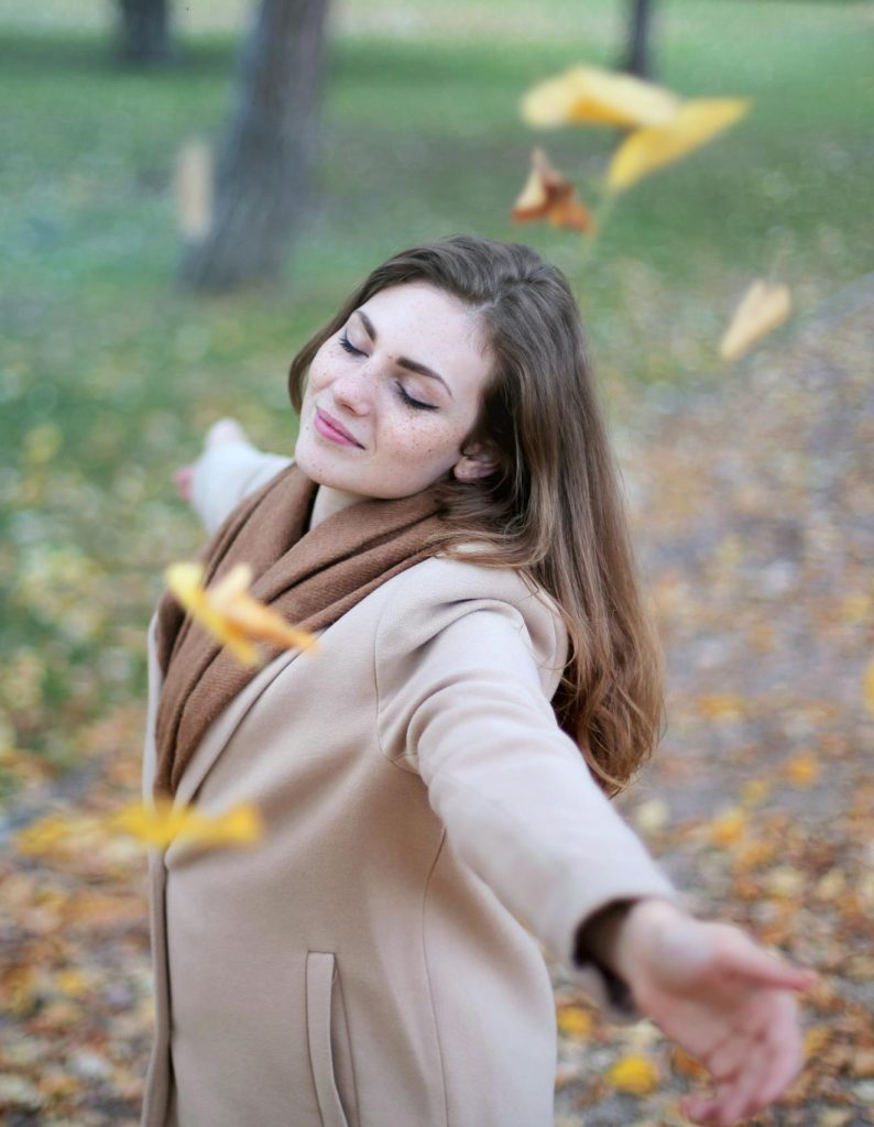 Young woman with arms outstretched, delighting in fallen leaves in a Paris park during autumn daytime.